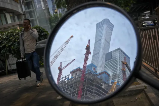 رجل يسير بالقرب من مرآة مجنّحة تعكس موقع بناء في منطقة الأعمال المركزية ببكين (رويترز)