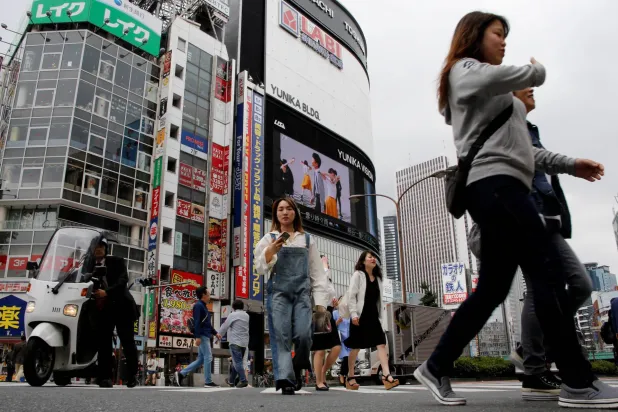 أشخاص يعبرون أحد الشوارع في منطقة شينغوكو للتسوق والأعمال في طوكيو (رويترز)