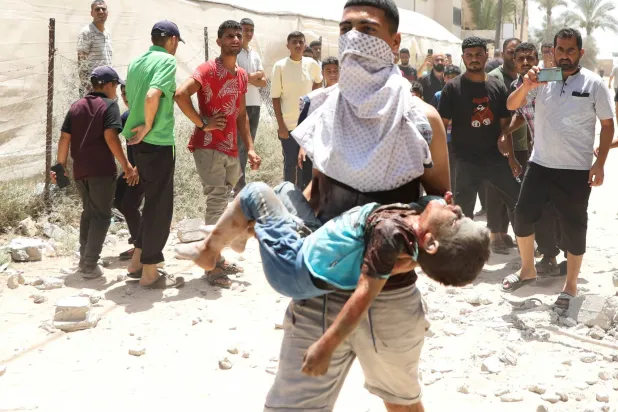 فلسطيني يحمل طفلاً أصيب بقصف إسرائيلي في دير البلح الجمعة (رويترز)