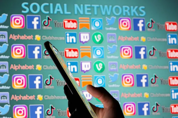 صورة تظهر امرأة تحمل هاتفاً ذكياً أمام شعارات وسائل التواصل الاجتماعي في 25 مايو 2021 (رويترز)