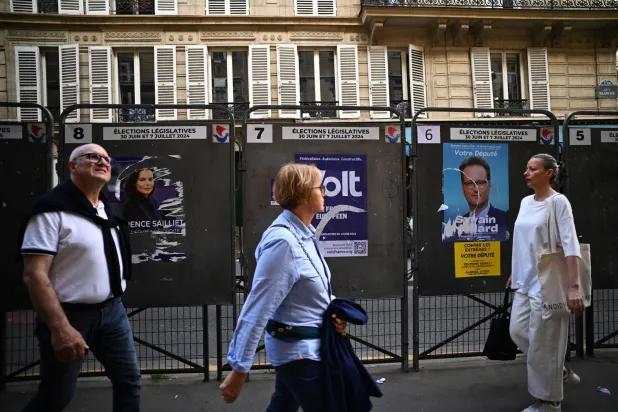 فرنسيون يسيرون أمام ملصقات انتخابية خارج مركز اقتراع في باريس السبت (رويترز)