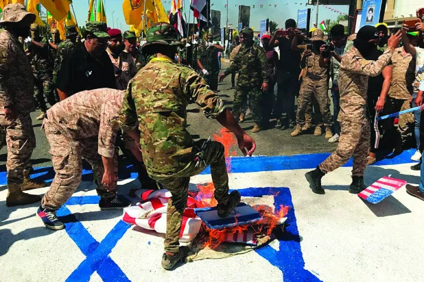 
عناصر فصيل عراقي مقرب من طهران يحرقون علم إسرائيل في أحد شوارع بغداد (أ.ب)