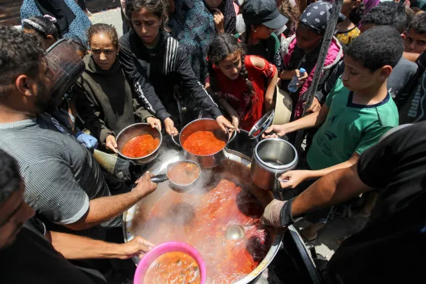 فلسطينيون يهرعون لتلقي الطعام من مطبخ خيري وسط نقص إمدادات المساعدات في خان يونس (رويترز)