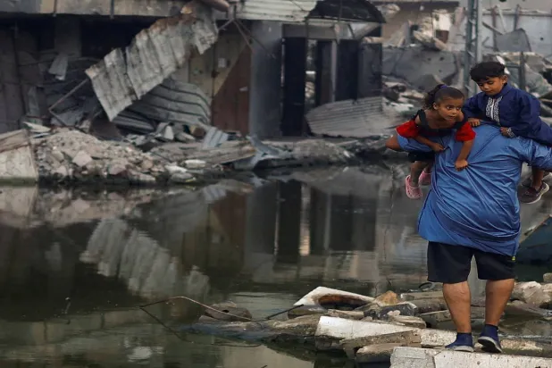 فلسطيني يحمل أطفاله وسط مبان دمرتها غارة إسرائيلية في خان يونس (رويترز)

