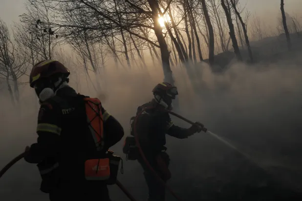 رجال الإطفاء يكافحون النيران خلال حريق غابات في منطقة سكنية في ستاماتا بالقرب من أثينا (إ.ب.أ)