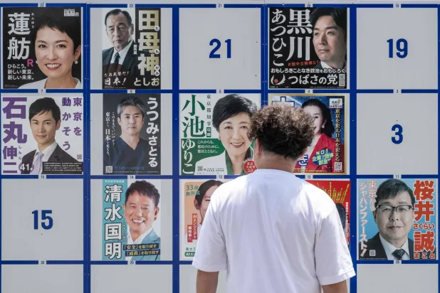 رجل يمر أمام لافتة تحمل صور المرشحين لانتخابات حاكم طوكيو (أ.ف.ب)