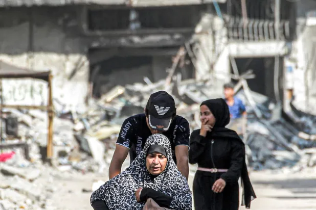 فلسطيني يدفع امرأة على كرسي متحرك يوم الاثنين في أحد شوارع خان يونس بقطاع غزة (أ.ف.ب)