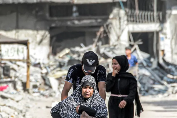 Bir Filistinli dün (pazartesi) Gazze Şeridi'nin Han Yunus kentindeki bir caddede tekerlekli sandalyedeki kadını itiyor. (AFP)