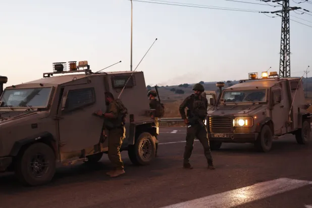 شرطة وجنود إسرائيليون يغلقون طريقاً بينما يتصاعد الدخان في الخلفية بعد إصابة شخصين في سقوط صاروخ بمرتفعات الجولان (إ.ب.أ)