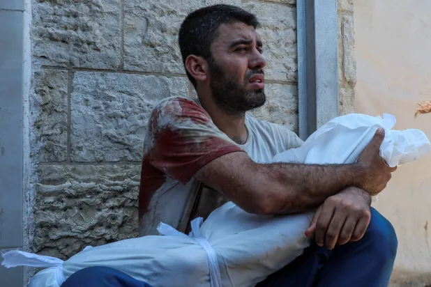 أب فلسطيني يحمل جثمان ولده الذي قُتل في غارة إسرائيلية بمستشفى شهداء الأقصى أمس (رويترز)