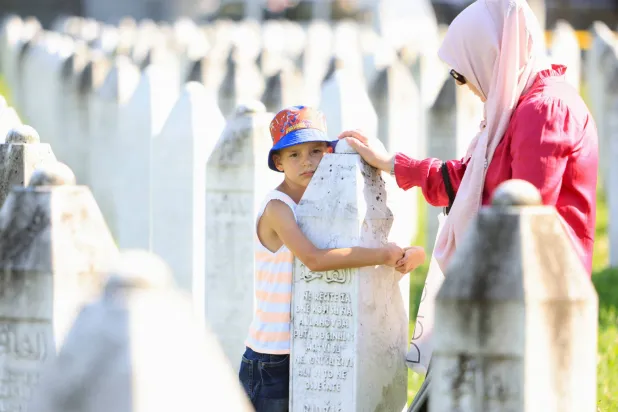 طفل بوسني يحضن شاهد قبر قرب أمه في المقبرة التذكارية لضحايا المجزرة ببوتوكاري الخميس (رويترز)