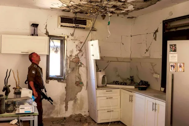 Kiryat Shmona'ya atılan bir Hizbullah roketinin isabet ettiği evdeki hasarı inceleyen İsrail askeri (AFP)