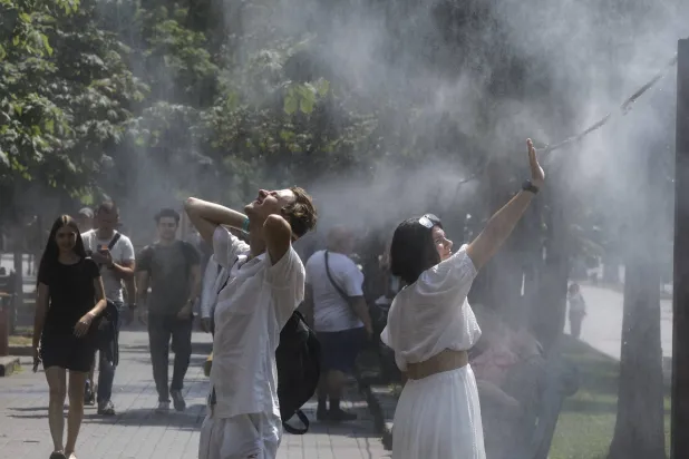 أوكرانيون يبردون أنفسهم بالمياه المرشوشة من الأنابيب المعلقة فوق رصيف بالشارع المركزي في خريشاتيك (إ.ب.أ)