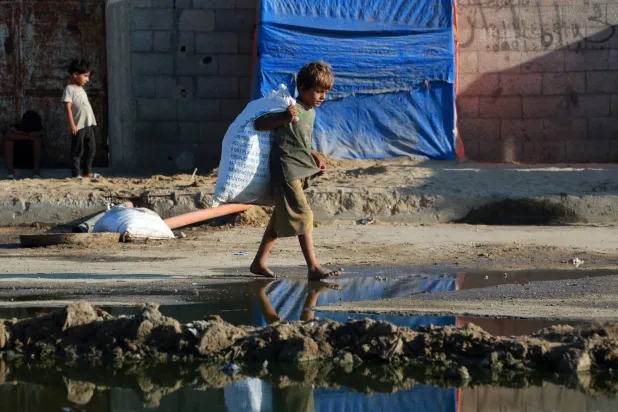 صبي فلسطيني صغير يسير حافي القدمين بالقرب من مياه الصرف الصحي الراكدة في دير البلح بوسط قطاع غزة (أ.ف.ب)
