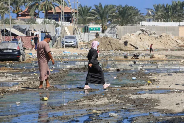 فلسطينيون يعبرون شارعاً غمرته مياه الصرف الصحي في دير البلح وسط قطاع غزة (أ.ف.ب)