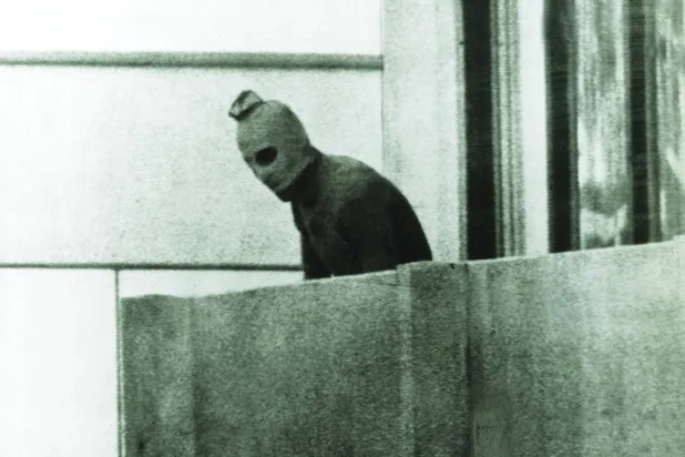 
أحد منفّذي عملية ميونيخ يطلّ من مقر البعثة الإسرائيلية في القرية الأولمبية (غيتي)