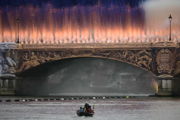 قارب يحمل الشعلة الأولمبية أمام جسر على نهر السين خلال افتتاح أولمبياد باريس 2024 (أ.ف.ب)