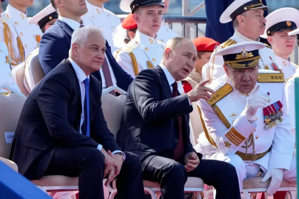 الرئيس الروسي فلاديمير بوتين يجلس أمام وزير الدفاع وقائد البحرية بمناسبة الاحتفالات بيوم البحرية في سان بطرسبرغ الأحد (رويترز)