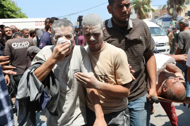 رجل فلسطيني مصاب يغطي وجهه بينما يسير معه آخر عقب غارة إسرائيلية على دير البلح (رويترز)