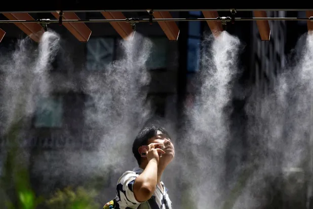 رجل يأخذ استراحة تحت رذاذ المياه بينما أصدرت الحكومة اليابانية تحذيرات من ضربات الشمس في طوكيو (رويترز)