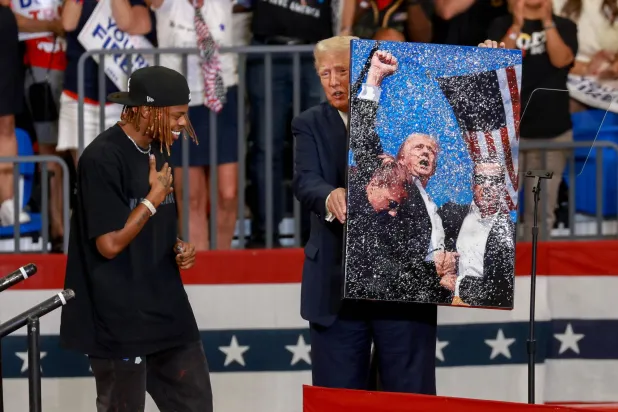 المرشح الجمهوري للرئاسة الرئيس الأميركي السابق دونالد ترمب يحمل عملاً فنياً وقعه للفنان لوال إيزواجبي يتناول محاولة اغتيال ترمب في تجمع انتخابي بمركز مؤتمرات جامعة ولاية جورجيا في 3 أغسطس 2024، في أتلانتا (أ.ف.ب)