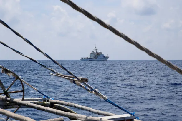 سفينة خفر سواحل صينية تظهر من قارب صيد فلبيني في منطقة سكاربورو شول المتنازع عليها في بحر الصين الجنوبي (رويترز)