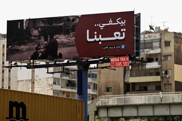 A man walks on an overpass beneath a giant billboard that reads "Enough, we are tired, Lebanon doesn't want war" on a street in Beirut on August 7, 2024, amid regional tensions during the ongoing war between Israel and the Palestinian Hamas movement in the Gaza Strip. (AFP)