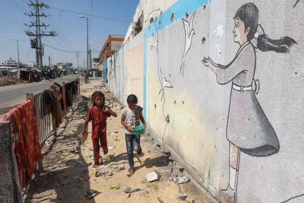 فتيات فلسطينيات يتجولن أمام جدارية في مخيم مؤقت للنازحين في دير البلح وسط قطاع غزة في 13 أغسطس 2024 (أ.ف.ب)