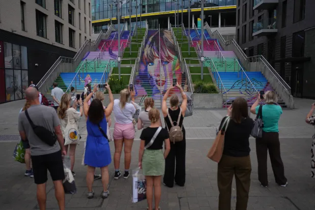 يلتقط عشاق المغنية الأميركية تايلور سويفت صوراً لجدارية في ويمبلي قبل حفل جولتها الموسيقية 14 أغسطس 2024 (د.ب.أ)