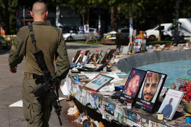 جندي إسرائيلي يمشي أمام صور تذكارية للرهائن في تل أبيب (رويترز)