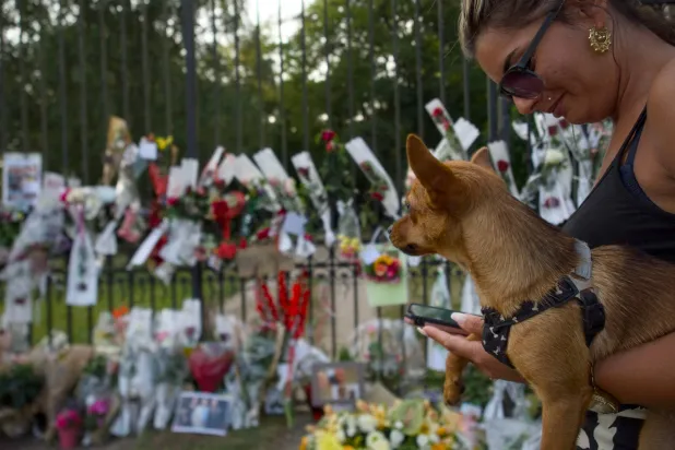 امرأة تحمل كلباً جاءت لتكريم الممثل الفرنسي الراحل آلان ديلون عند بوابة مدخل ملكية ديلون لا بروليري في دوشي وسط فرنسا 19 أغسطس 2024 (أ.ف.ب)