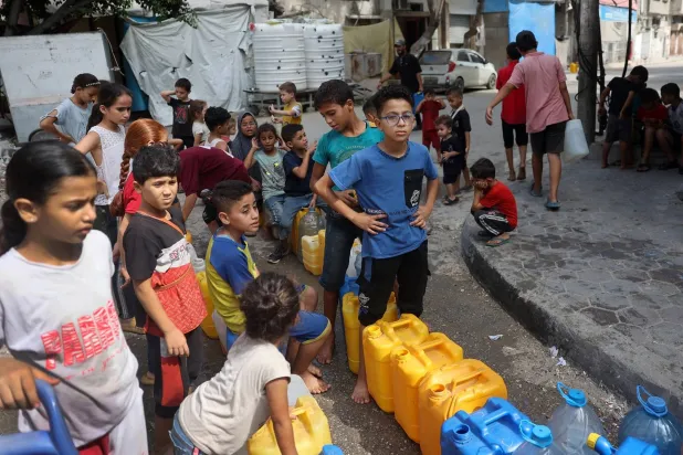 أطفال فلسطينيون يصطفون عند نقطة توزيع المياه في مخيم البريج للاجئين وسط غزة (أ.ف.ب)