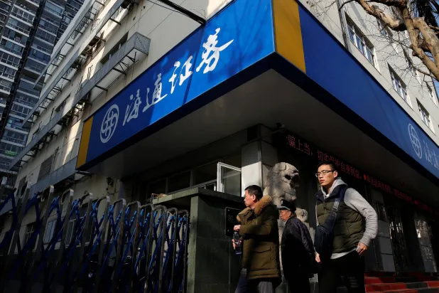 أشخاص يمشون أمام فرع شركة هايتونغ للأوراق المالية في شنغهاي (رويترز)