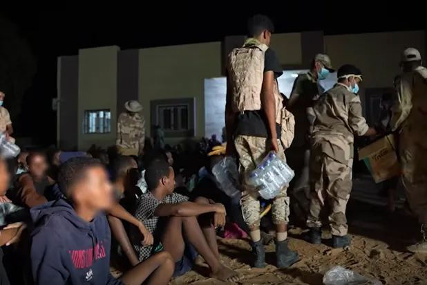 جنود يوزعون زجاجات مياه على مجموعة كانت محتجَزة لدى تجار البشر في ليبيا (لقطة من فيديو نشره النائب العام الليبي)