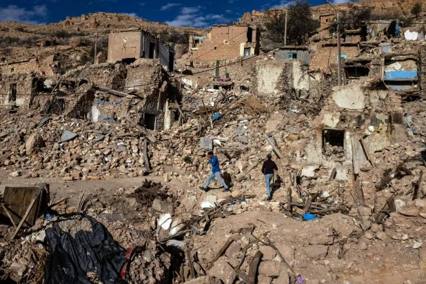 يسير أشخاص وسط أنقاض المباني المدمرة في قرية دوزرو التي ضربها الزلزال في وسط المغرب في 13 فبراير 2024 (أ.ف.ب)