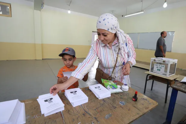 سيدة جزائرية وإلى جوارها طفل في أثناء مشاركتها (السبت) في الانتخابات الرئاسية بالبلاد (إ.ب.أ)