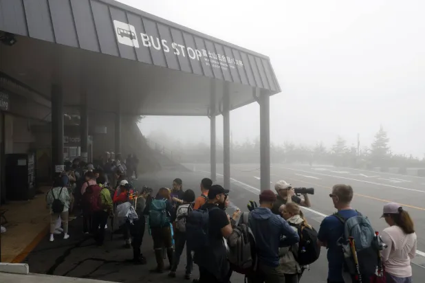سائحون يصطفّون لركوب الحافلة خلال مغادرة جبل فوجي باليابان (إ.ب.أ)
