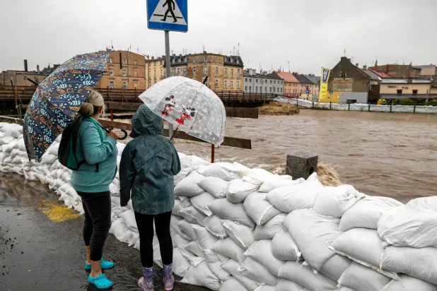 أشخاص ينظرون إلى مياه الفيضان جنوب بولندا من خلف سد بأكياس الرمل (رويترز)