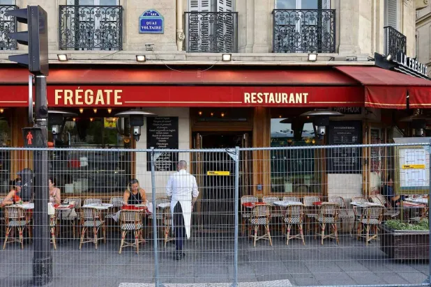 يجلس الناس في مطعم بينما يُنشر سياج الأمن المحيط بالاحتفال الافتتاحي قبل دورة الألعاب الأولمبية والبارالمبية بباريس (رويترز)