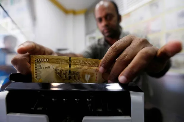 رجل يعد الروبية السريلانكية باستخدام آلة عد النقود في مكتب صرف أموال في كولومبو (رويترز)