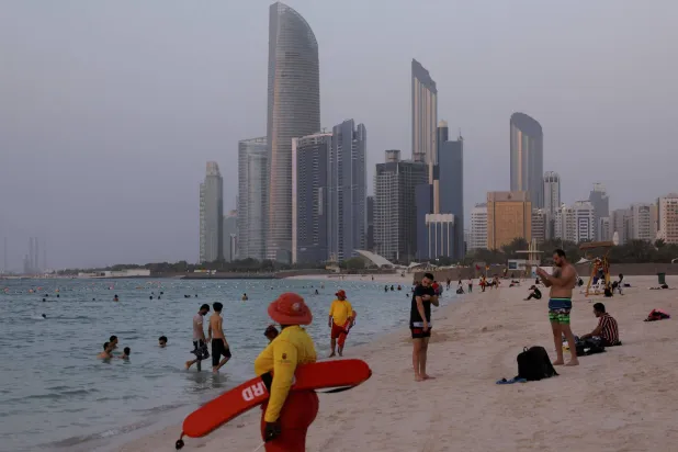 يستمتع الناس بالشاطئ حيث تظهر أبوظبي في الخلفية (رويترز)