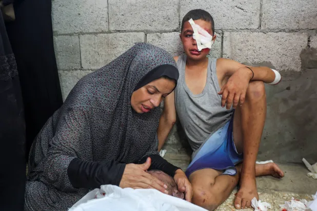 طفل فلسطيني وشقيقته يبكيان أمام جثمان والدهما الذي قُتل بغارة إسرائيلية في دير البلح بوسط قطاع غزة الأربعاء (رويترز)