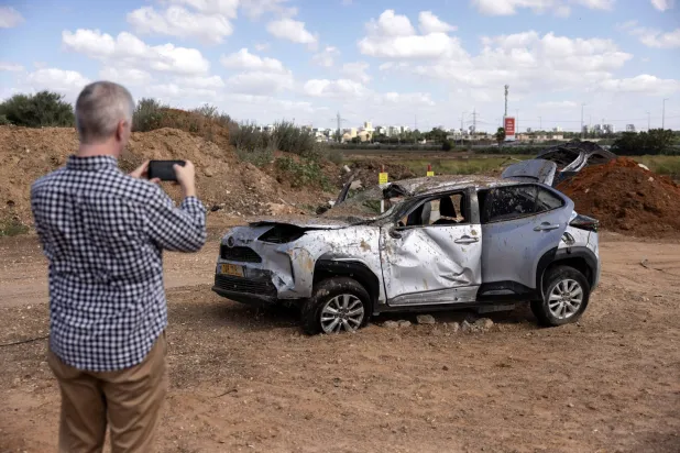 رجل يلتقط صورة لسيارة تضررت في المنطقة التي سقط فيها صاروخ باليستي إيراني في تل أبيب (رويترز)