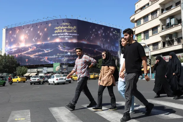إيرانيون يسيرون أمام لوحة دعائية تصور الهجوم الصاروخي الأخير على إسرائيل وعبارة باللغة الفارسية تقول: «إذا كنت تريد الحرب فنحن سادة الحرب» في ساحة انقلاب (الثورة) وسط طهران (إ.ب.أ)