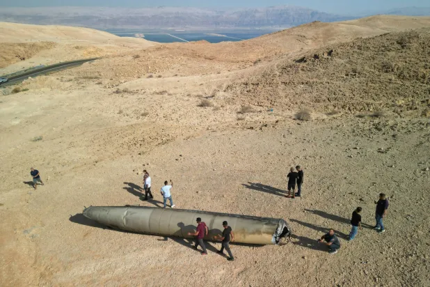 صورة التقطها طائرة مُسيرة تُظهر أشخاصاً يقفون حول بقايا صاروخ باليستي بالصحراء بعد هجوم إيران على إسرائيل (رويترز)