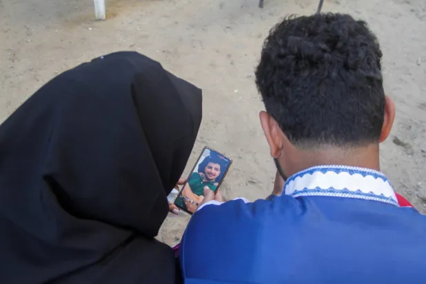 سيدة فلسطينية تبحث عن ابنها المفقود عبر صورته على هاتفها في مخيم جباليا (رويترز)