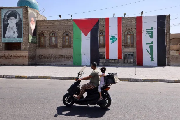 دراجة تعبر شارعاً ببغداد وقد رفعت فيه أعلام العراق ولبنان وفلسطين (أ.ف.ب)