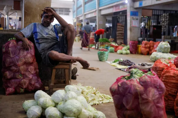 بائع ينتظر الزبائن في كشك الخضر الخاص به بسوق رئيسية بكولومبو (رويترز)