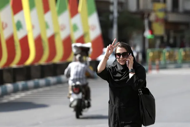 امرأة إيرانية ترفع علامة النصر أثناء مرورها بجانب أعلام إيران ولبنان و«حزب الله» في أحد شوارع طهران اليوم (إ.ب.أ)