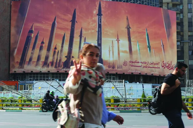 امرأة غير محجبة تمر أمام لافتة دعائية للصواريخ الإيرانية في ساحة «ولي عصر» وسط طهران (أرشيفية - رويترز)